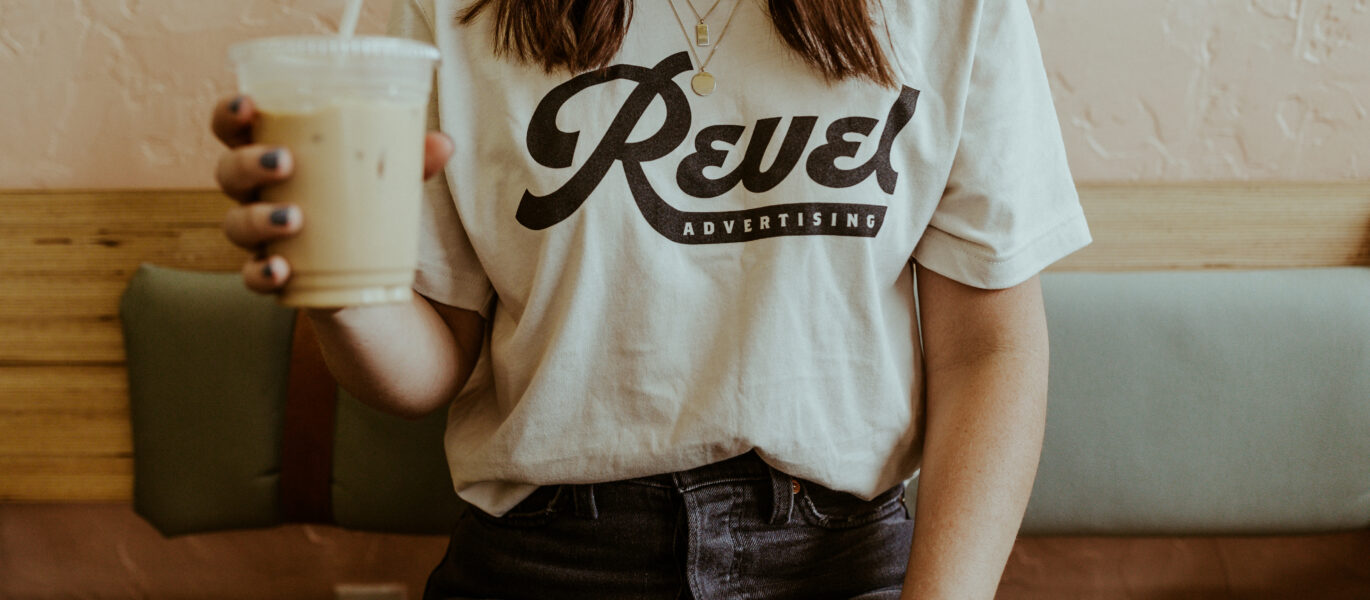 Woman wearing a Revel Advertising t-shirt holding a cup of coffee